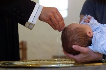 Spædbarn døbes af præsten